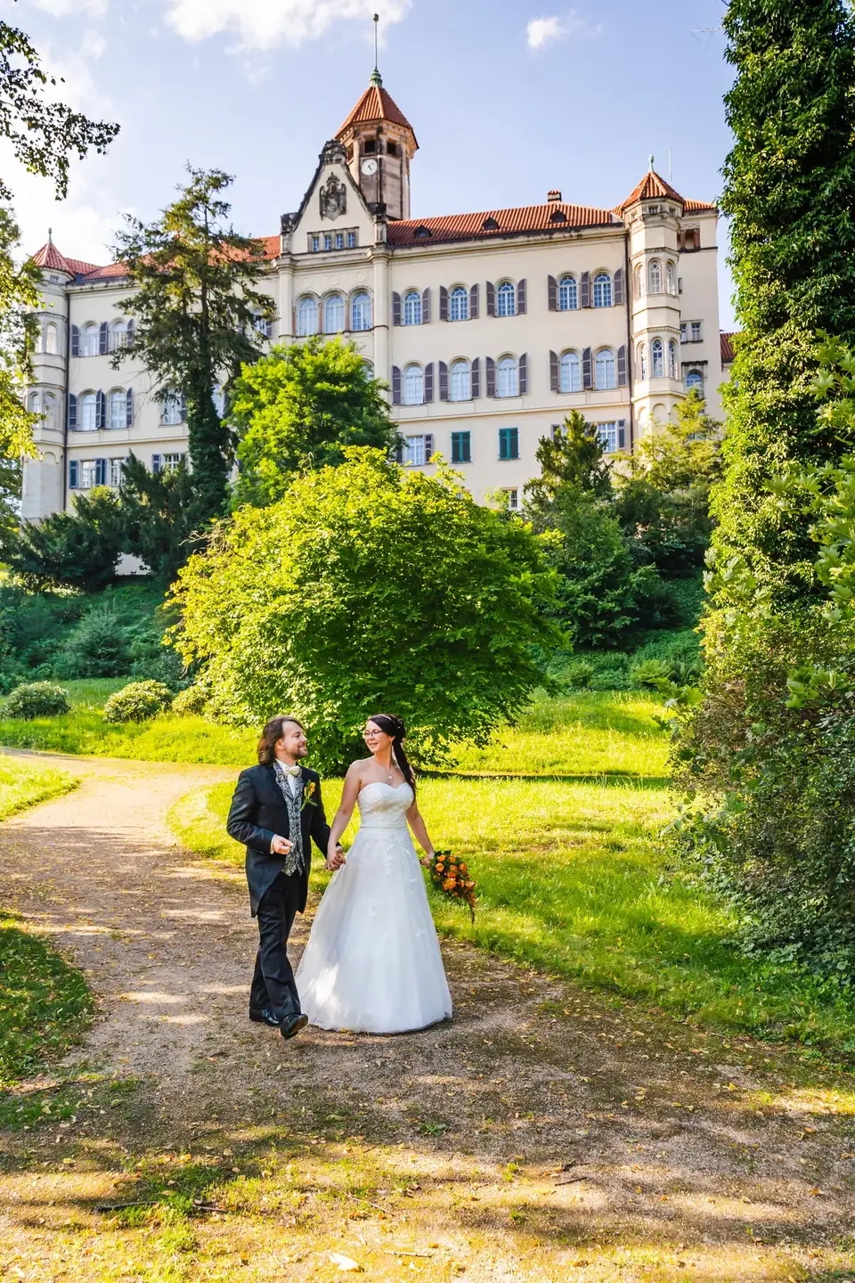 Brautpaar geht Hand in Hand durch den Park vor einem Schloss